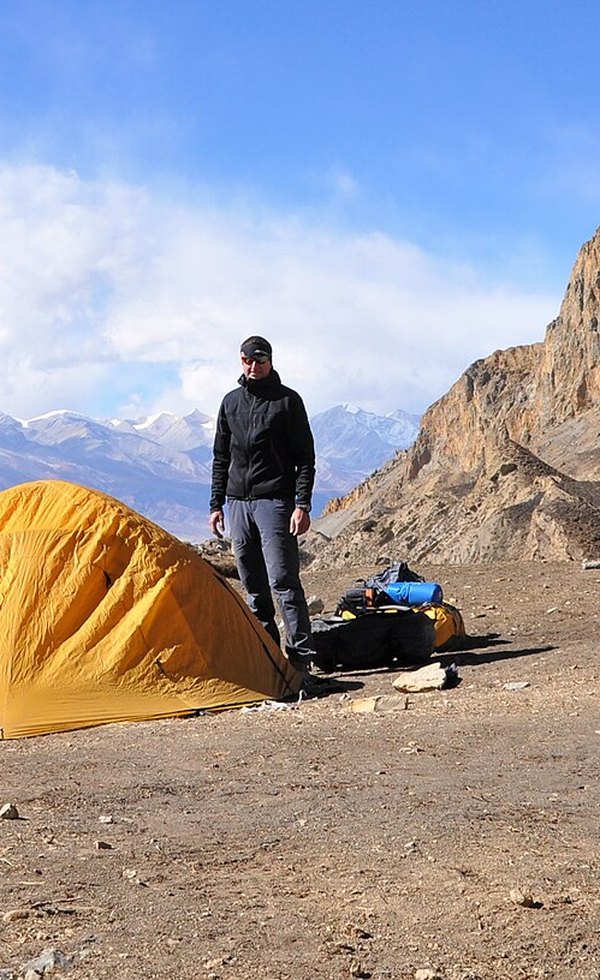 Trekker next to a tent in a remote mountain valley